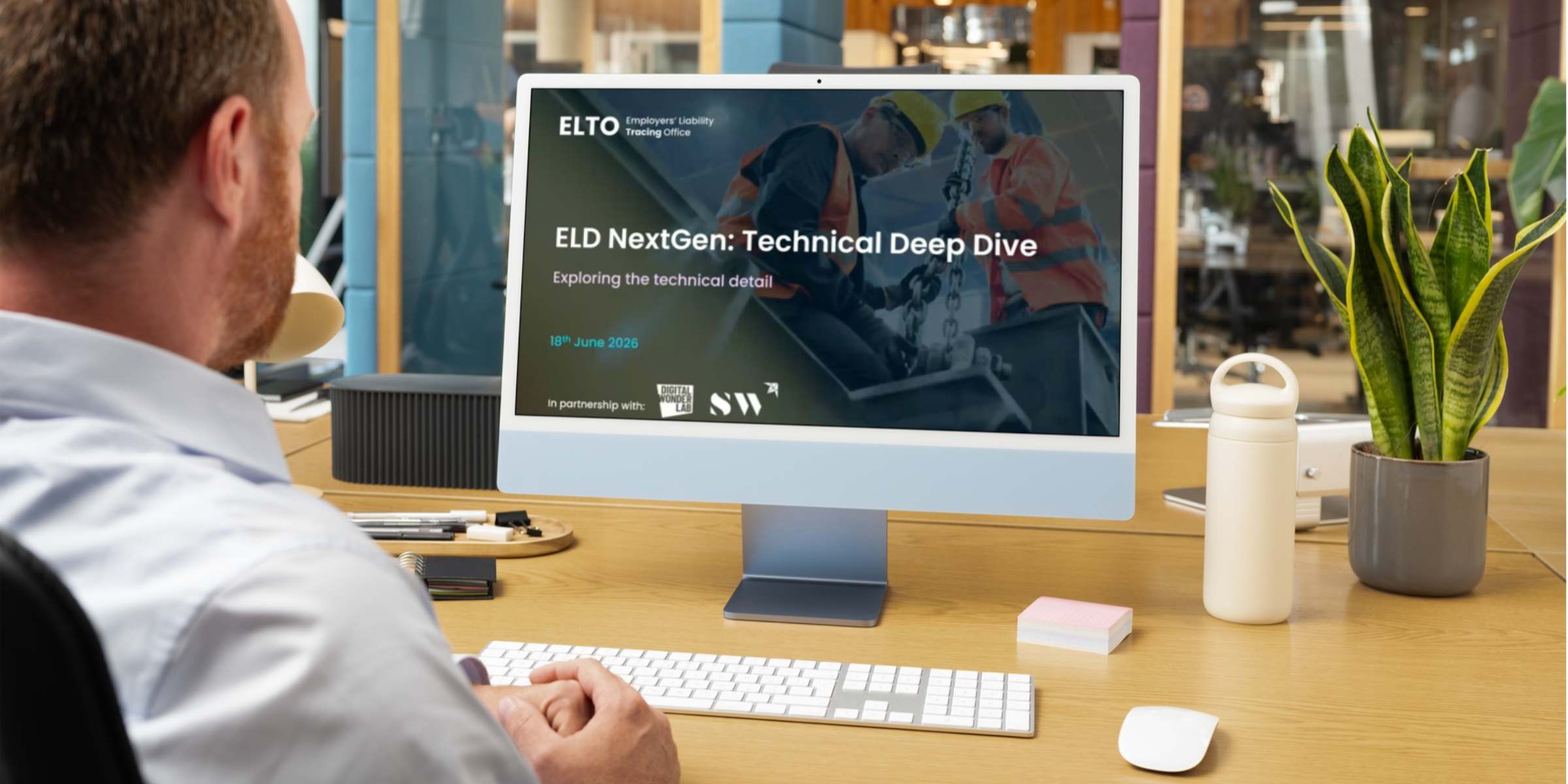 A person sits at a desktop computer, with multiple individuals visible on the screen, engaged in a virtual meeting or discussion.