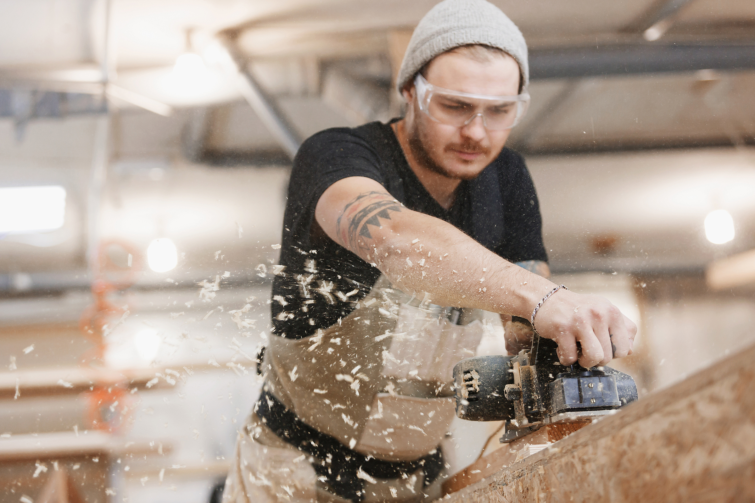 A man operates a circular saw, cutting through a piece of wood in a workshop setting.