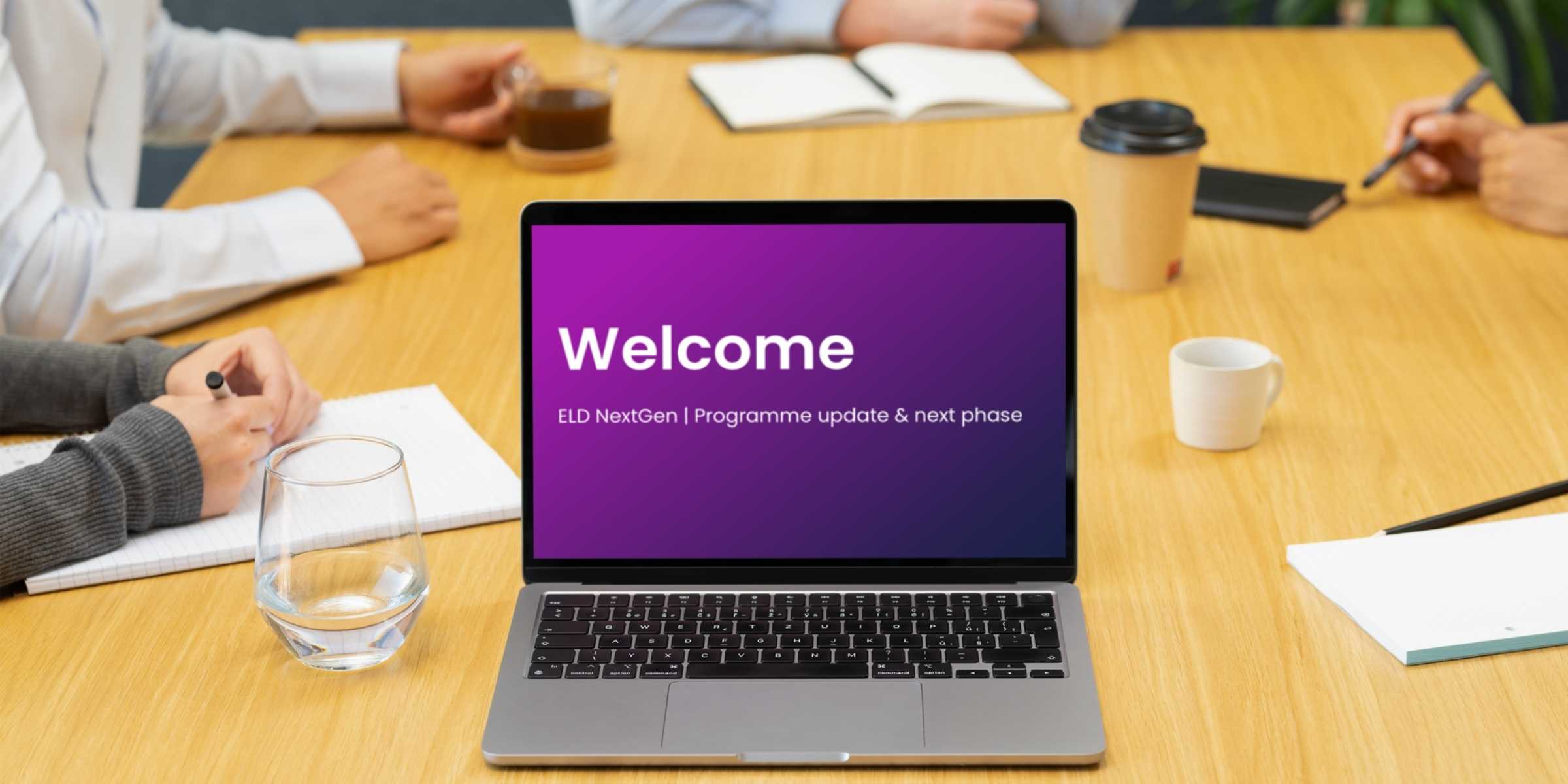 Welcome screen displayed on a laptop in a meeting room, featuring a company logo and a prompt to join the meeting.