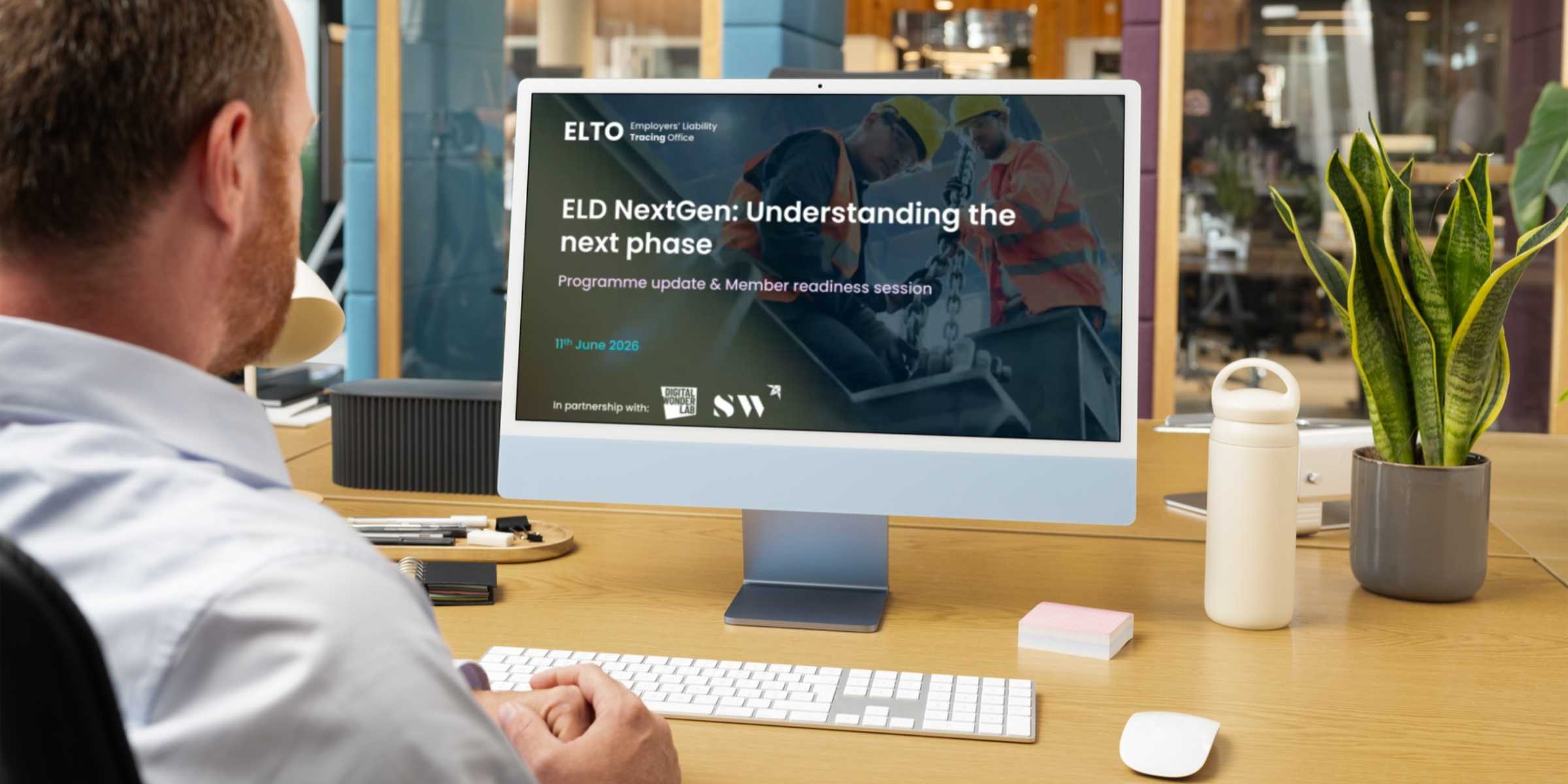 A person sits at a desktop computer, with multiple individuals visible on the screen, engaged in a virtual meeting or discussion.